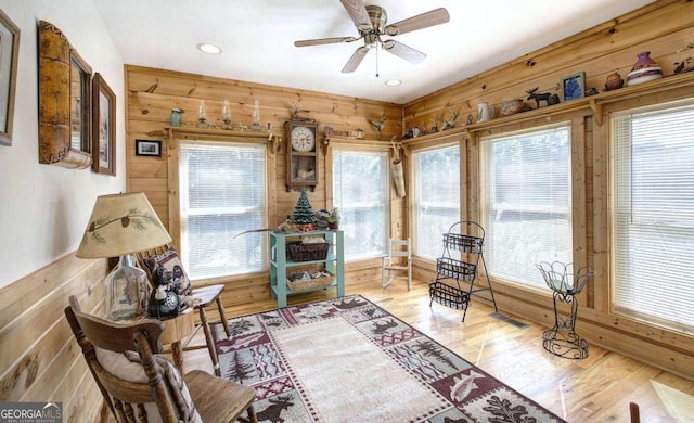 sitting room with wood walls, light hardwood / wood-style floors, and ceiling fan