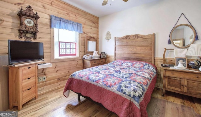 bedroom with ceiling fan, light hardwood / wood-style flooring, and wood walls