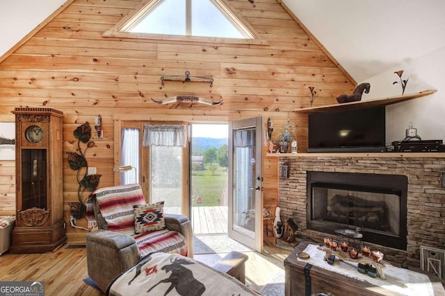 living room featuring a stone fireplace, wooden walls, light wood-type flooring, and high vaulted ceiling