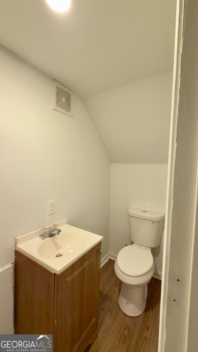 bathroom featuring hardwood / wood-style flooring, vanity, lofted ceiling, and toilet