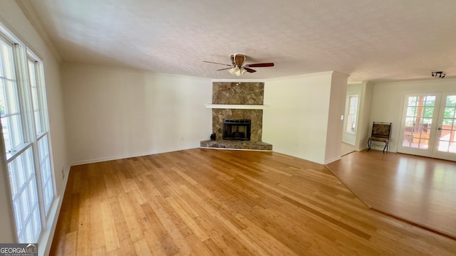 unfurnished living room featuring ceiling fan, light hardwood / wood-style floors, a textured ceiling, a stone fireplace, and french doors