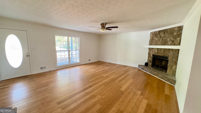 unfurnished living room featuring ceiling fan, a stone fireplace, wood-type flooring, and a textured ceiling