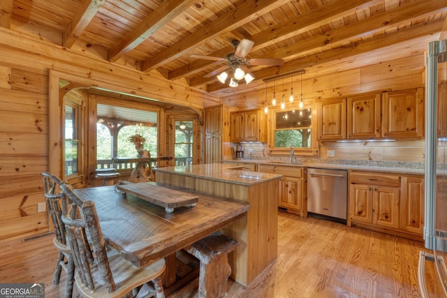 kitchen with light stone countertops, ceiling fan, decorative light fixtures, stainless steel dishwasher, and wooden walls