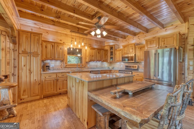 kitchen with ceiling fan, wood walls, light hardwood / wood-style flooring, stainless steel appliances, and a kitchen breakfast bar