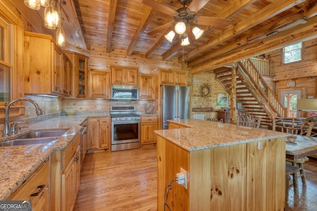 kitchen with a center island, ceiling fan with notable chandelier, stainless steel appliances, wooden walls, and light stone countertops