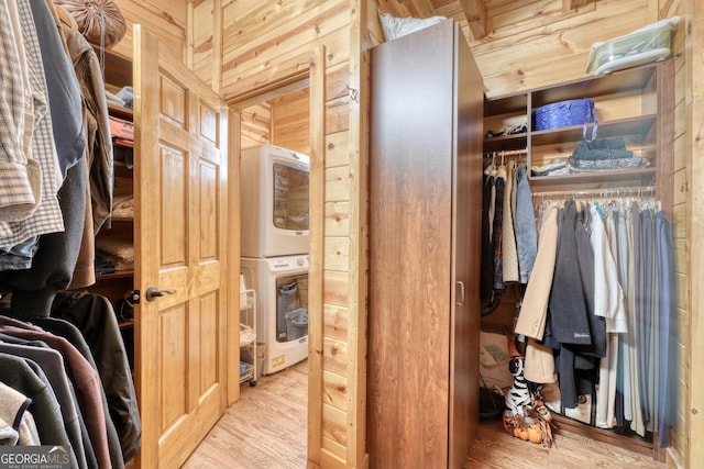 walk in closet with light wood-type flooring and stacked washer / drying machine