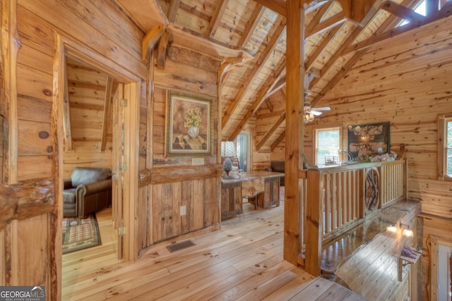 interior space featuring light hardwood / wood-style floors, beamed ceiling, wooden ceiling, ceiling fan, and wooden walls