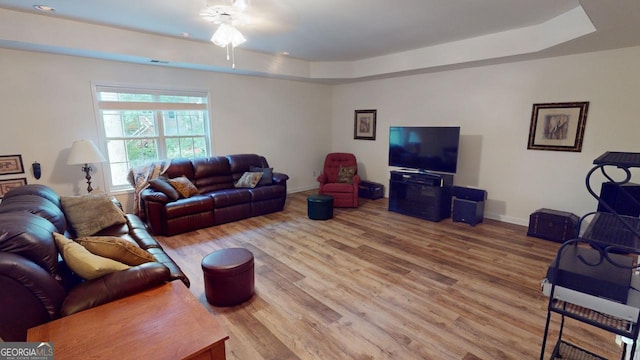 living room featuring ceiling fan, a raised ceiling, and wood-type flooring