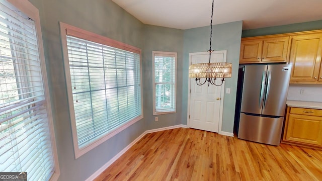 kitchen with light wood-type flooring, stainless steel refrigerator, decorative light fixtures, and a wealth of natural light