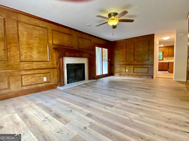 unfurnished living room with light hardwood / wood-style flooring, wood walls, ceiling fan, and ornamental molding