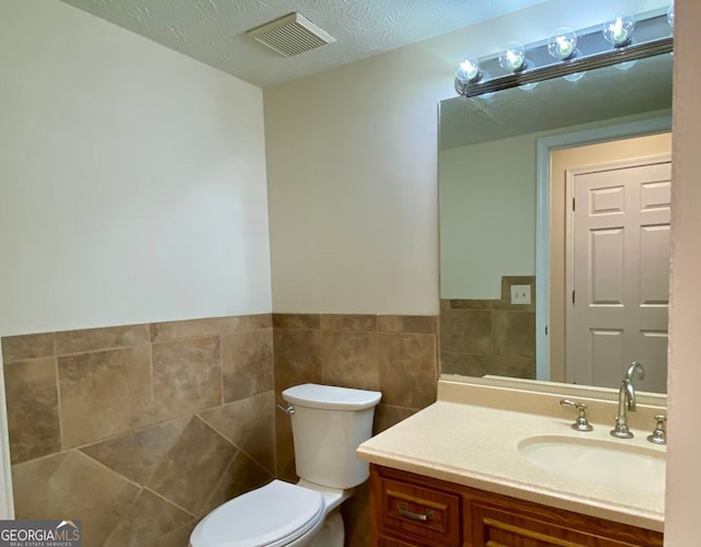 bathroom featuring vanity, tile walls, toilet, and a textured ceiling