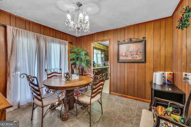 dining room with a notable chandelier, a healthy amount of sunlight, and wooden walls