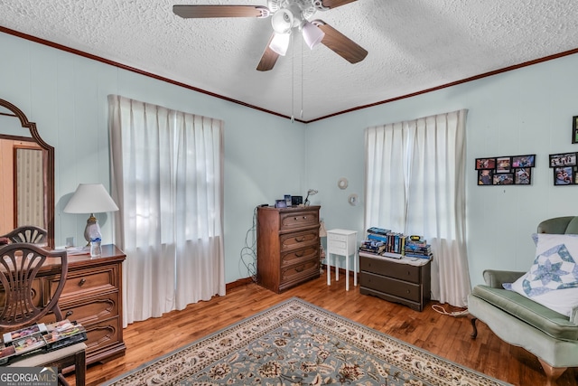 living area featuring ornamental molding, light wood-type flooring, ceiling fan, and a textured ceiling