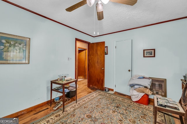 living area featuring ceiling fan, heating unit, light hardwood / wood-style flooring, ornamental molding, and a textured ceiling