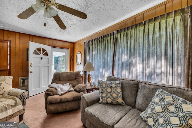 living room with ceiling fan, a textured ceiling, wooden walls, and carpet flooring