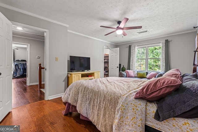 bedroom featuring a spacious closet, ornamental molding, dark hardwood / wood-style floors, and ceiling fan