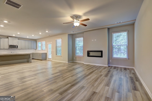 unfurnished living room with ceiling fan, light hardwood / wood-style flooring, and a wealth of natural light