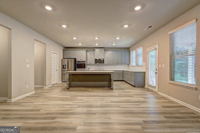 kitchen featuring gray cabinetry, stainless steel appliances, light hardwood / wood-style floors, and a center island with sink