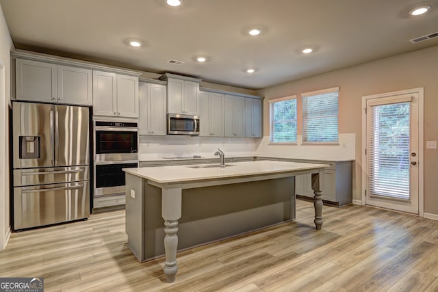 kitchen with light hardwood / wood-style floors, a breakfast bar, stainless steel appliances, a kitchen island with sink, and sink