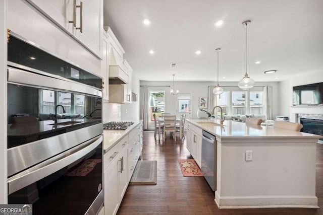 kitchen with white cabinets, a center island with sink, plenty of natural light, and stainless steel appliances