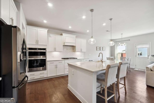 kitchen with a kitchen island with sink, dark wood-type flooring, white cabinets, stainless steel appliances, and decorative light fixtures