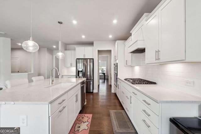 kitchen with white cabinets, a center island with sink, decorative light fixtures, appliances with stainless steel finishes, and dark hardwood / wood-style flooring