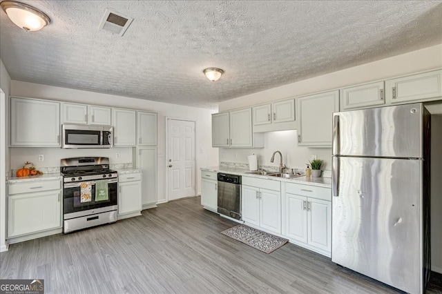 kitchen featuring light wood-type flooring, a textured ceiling, sink, white cabinetry, and stainless steel appliances