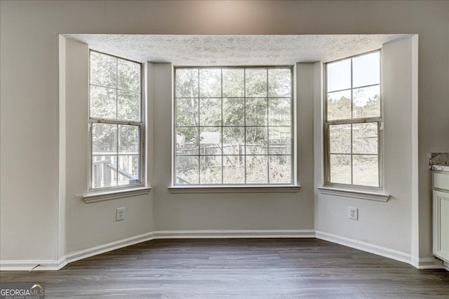 unfurnished dining area featuring a textured ceiling, dark hardwood / wood-style flooring, and a wealth of natural light