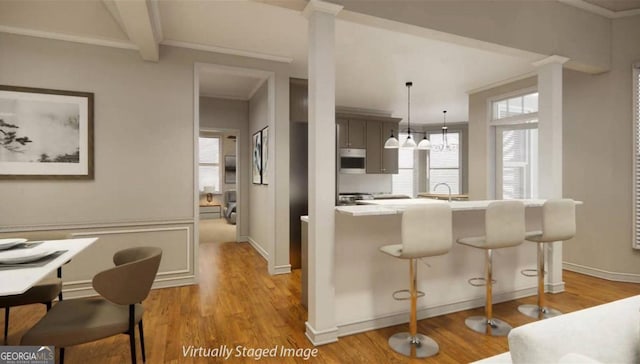 kitchen with hanging light fixtures, beam ceiling, gray cabinetry, a kitchen breakfast bar, and light wood-type flooring