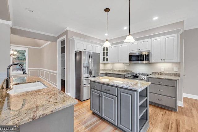 kitchen with sink, a kitchen island, white cabinetry, stainless steel appliances, and light wood-type flooring