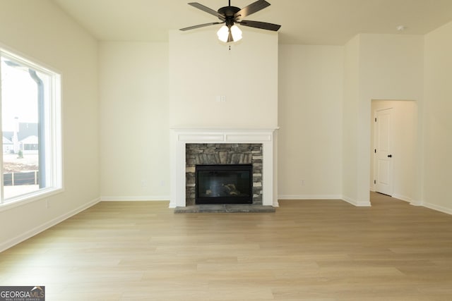 unfurnished living room with a stone fireplace, ceiling fan, and light wood-type flooring