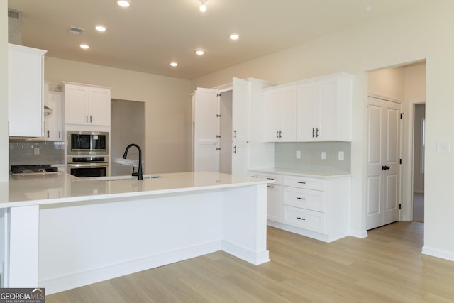 kitchen with backsplash, white cabinets, sink, light hardwood / wood-style floors, and stainless steel appliances