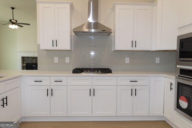 kitchen with stainless steel appliances, white cabinetry, wall chimney exhaust hood, and light hardwood / wood-style floors