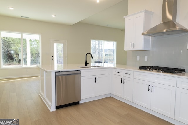 kitchen featuring sink, light hardwood / wood-style flooring, wall chimney exhaust hood, white cabinetry, and stainless steel appliances