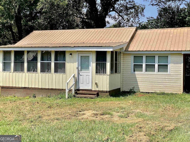 view of front facade with entry steps, metal roof, and a front lawn