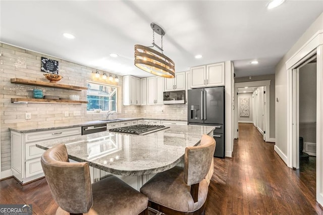 kitchen featuring a kitchen island, white cabinetry, stainless steel appliances, decorative light fixtures, and light stone counters