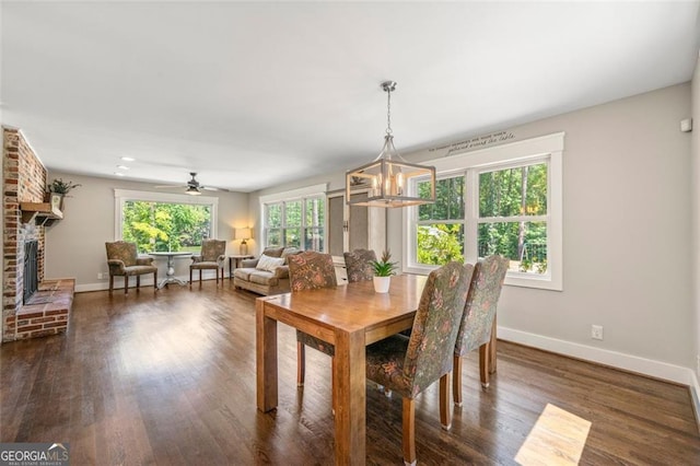 dining room with a brick fireplace, ceiling fan with notable chandelier, and dark hardwood / wood-style flooring