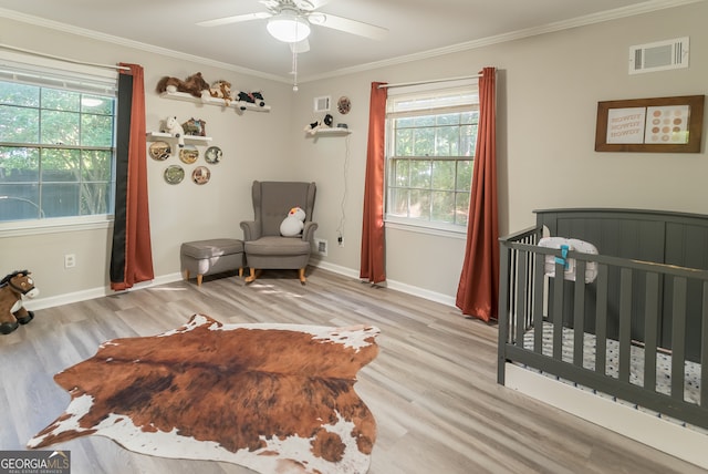 bedroom featuring a crib, crown molding, ceiling fan, and light hardwood / wood-style flooring