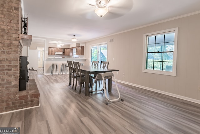 dining space with wood-type flooring, ceiling fan, a fireplace, and crown molding