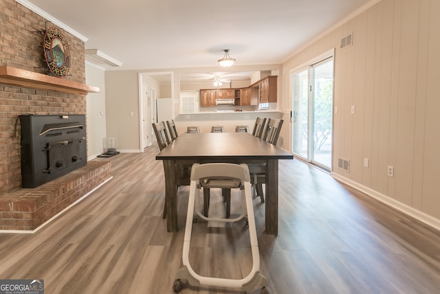 dining room with light wood-type flooring, ceiling fan, a fireplace, and crown molding