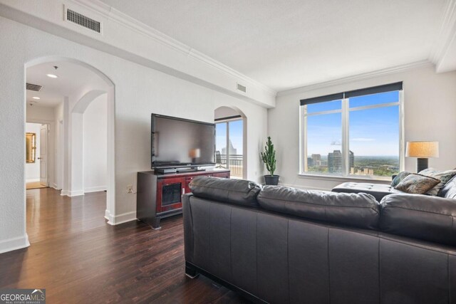 living room featuring arched walkways, dark wood-style flooring, crown molding, visible vents, and baseboards