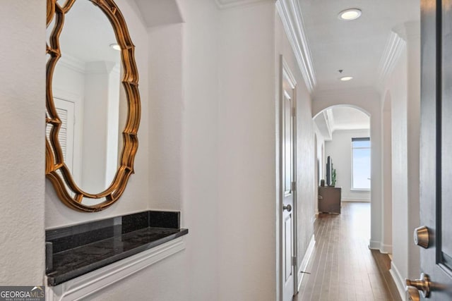 corridor with arched walkways, crown molding, recessed lighting, wood finished floors, and baseboards