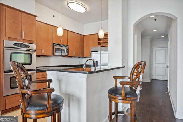 kitchen with arched walkways, stainless steel appliances, a kitchen bar, and brown cabinets