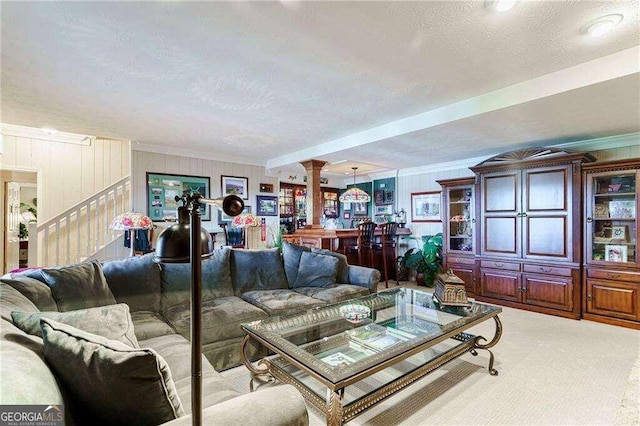 carpeted living room featuring bar area, a textured ceiling, crown molding, and ornate columns