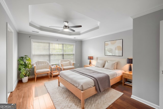 bedroom featuring dark wood-type flooring, ceiling fan, ornamental molding, and a tray ceiling