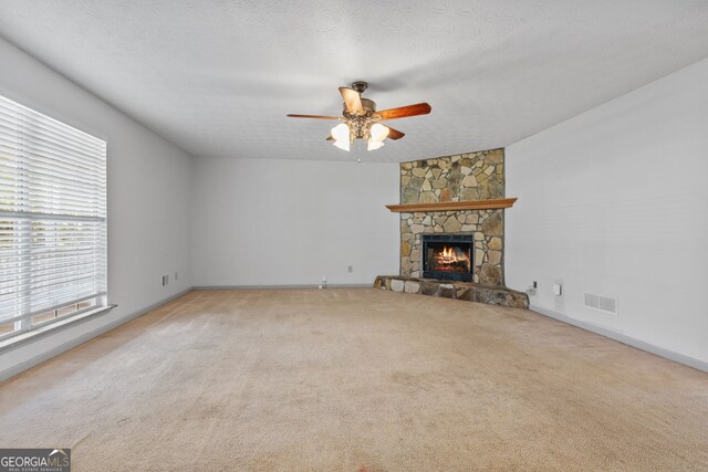 unfurnished living room with ceiling fan, light colored carpet, a textured ceiling, and a fireplace