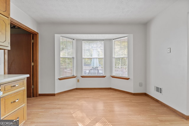 unfurnished dining area with a textured ceiling and light hardwood / wood-style flooring