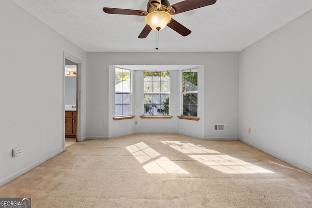 unfurnished bedroom featuring ceiling fan, a textured ceiling, ensuite bath, and light carpet