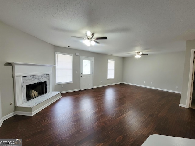 unfurnished living room with a textured ceiling, a fireplace, dark wood-type flooring, and ceiling fan