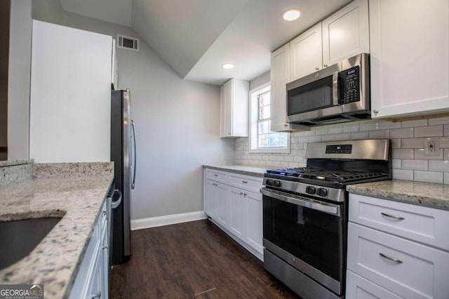 kitchen featuring appliances with stainless steel finishes, vaulted ceiling, dark wood-type flooring, white cabinets, and light stone countertops